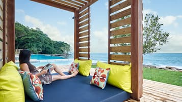 Une pergola en bois avec un coin salon agrémenté de coussins bleus, une piscine et une vue sur l’océan.