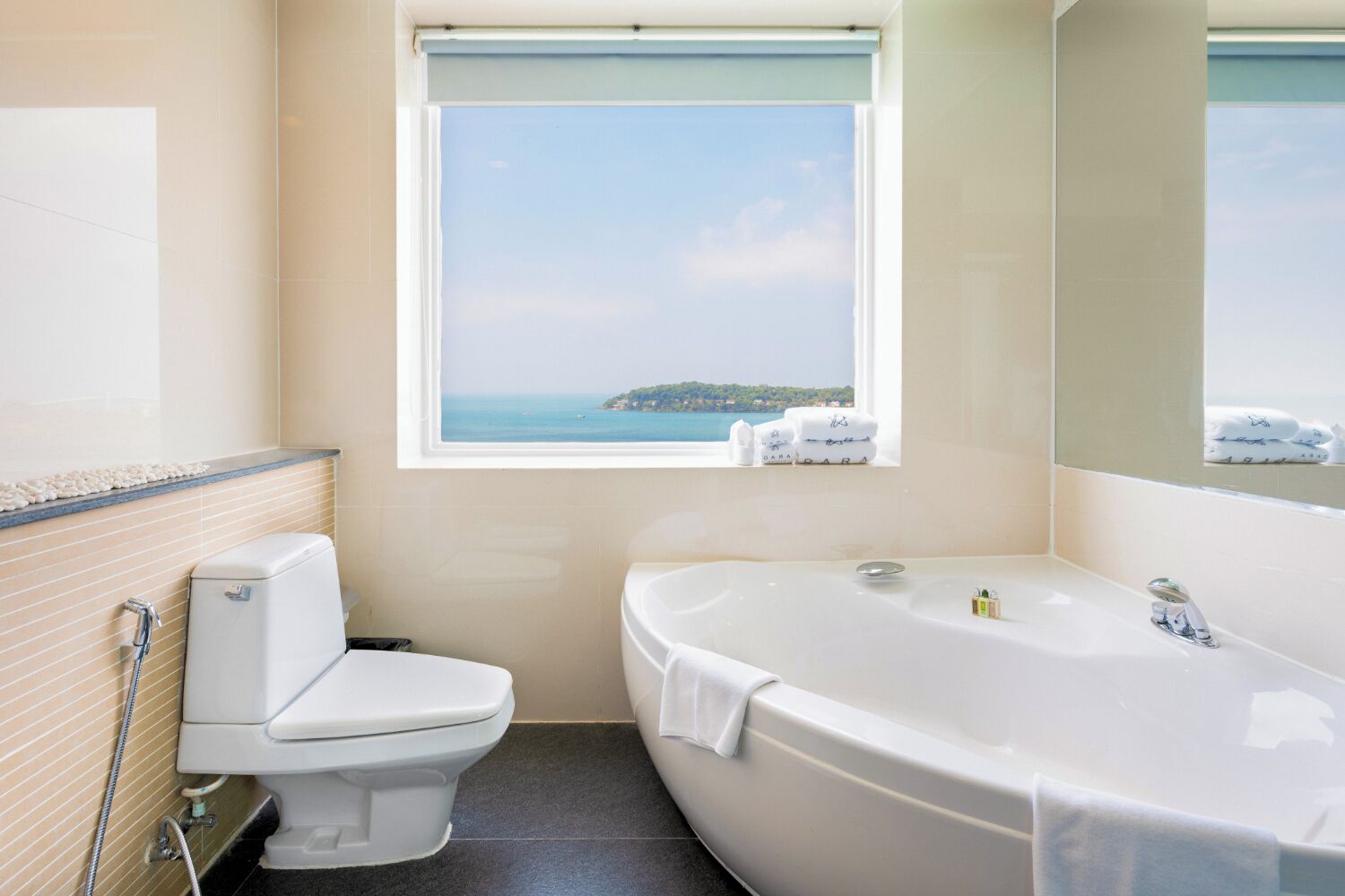 Un baño con inodoro, bañera y ventana con vista al mar.