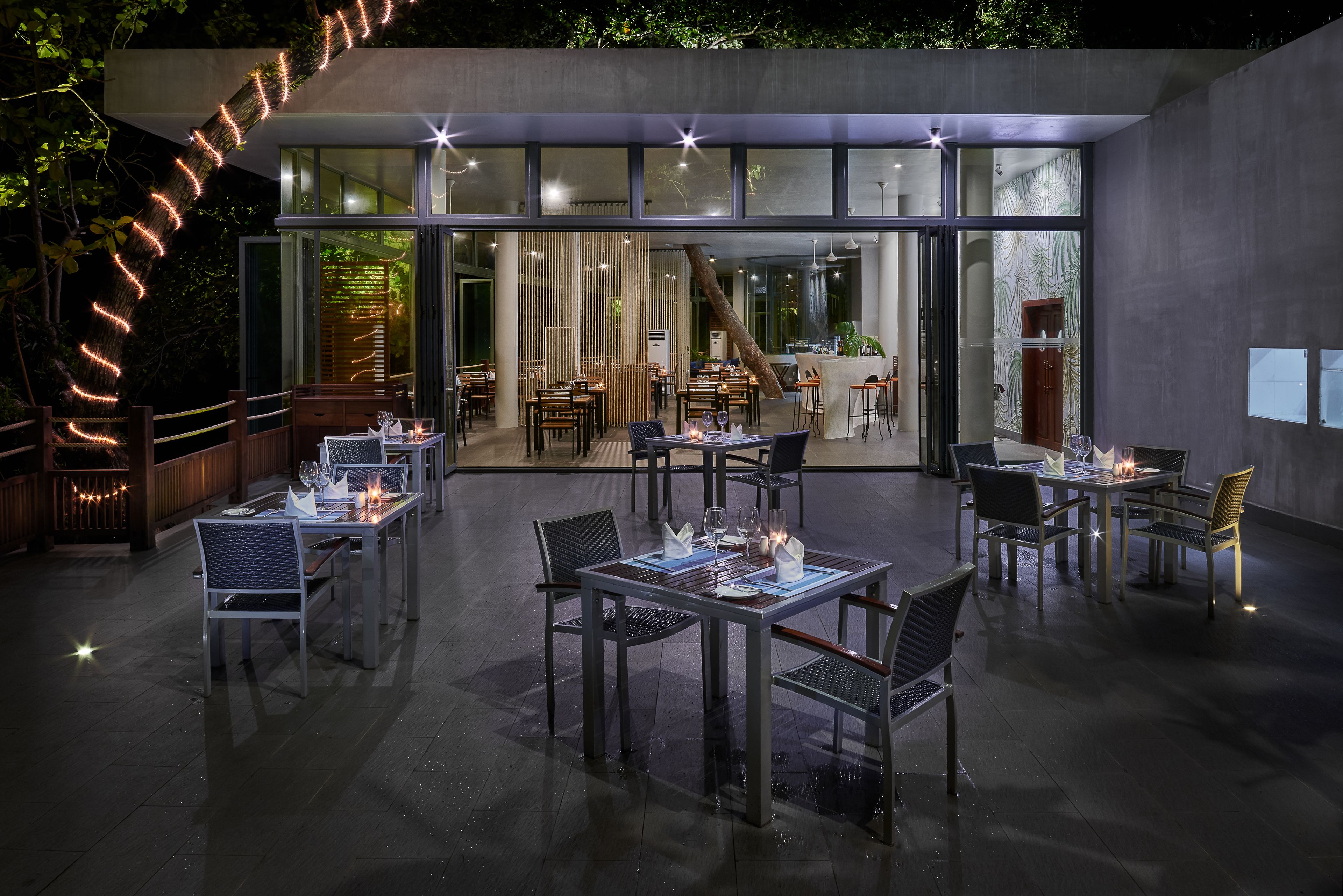 An outdoor dining area with tables and chairs, a wooden deck, and a glass-enclosed entrance.