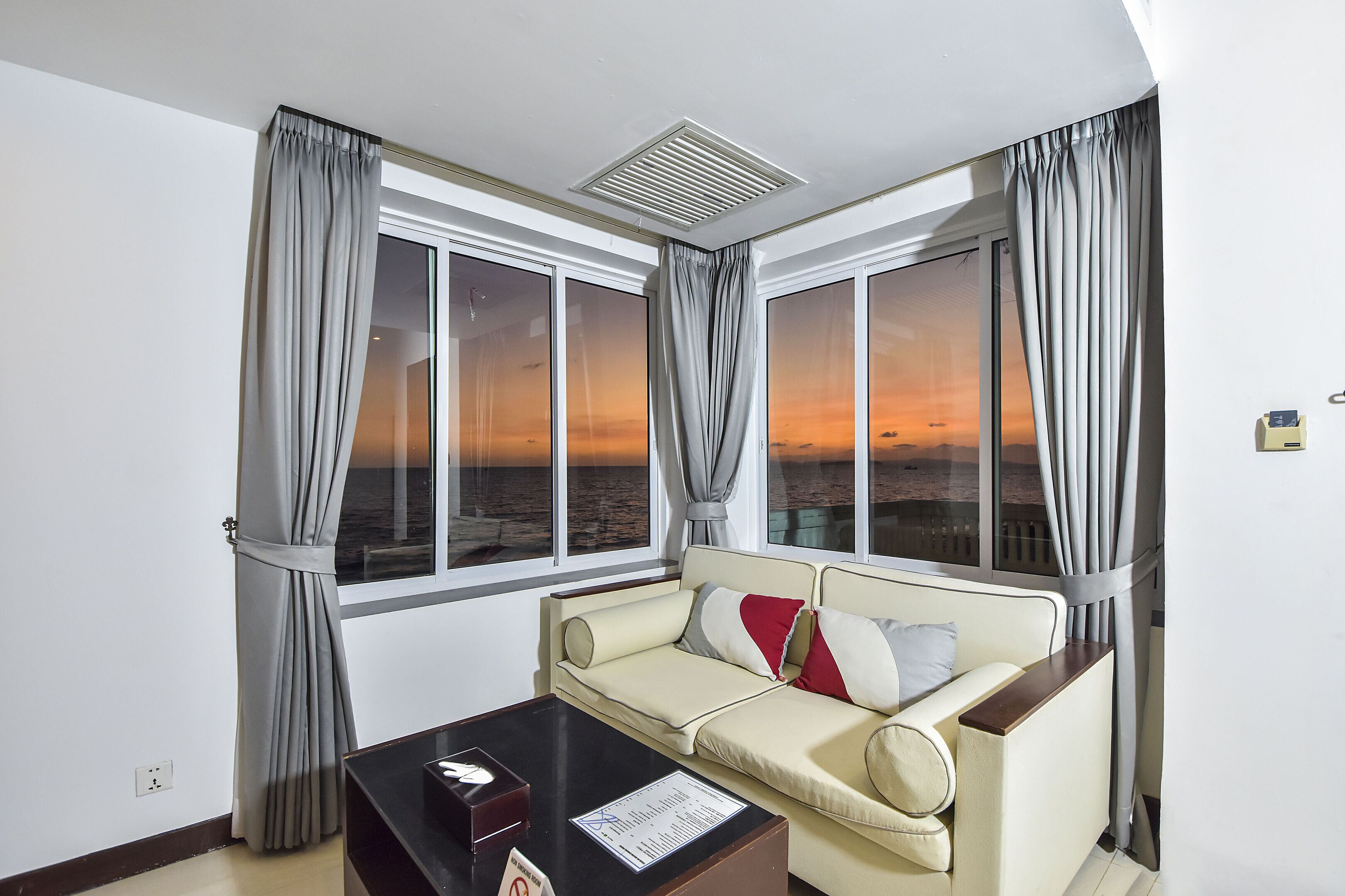 A room with a sofa, a table with a menu, and large windows with curtains.