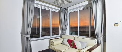 A room with a sofa, a table with a menu, and large windows with curtains.