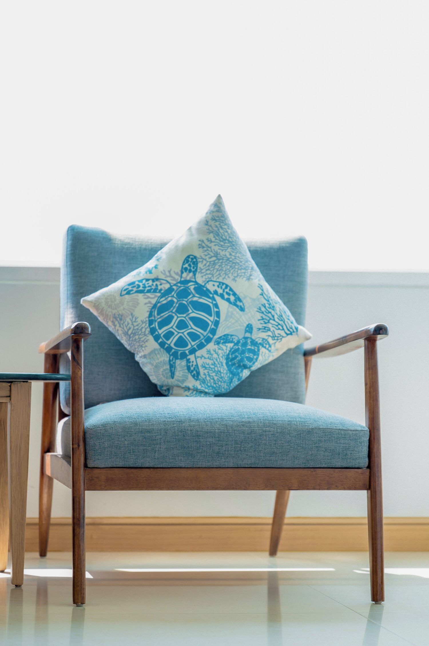 Ein Stuhl mit blauer Kissenauflage, die ein Meeresschildkröten-Design zeigt, vor einer schlichten Wand platziert.