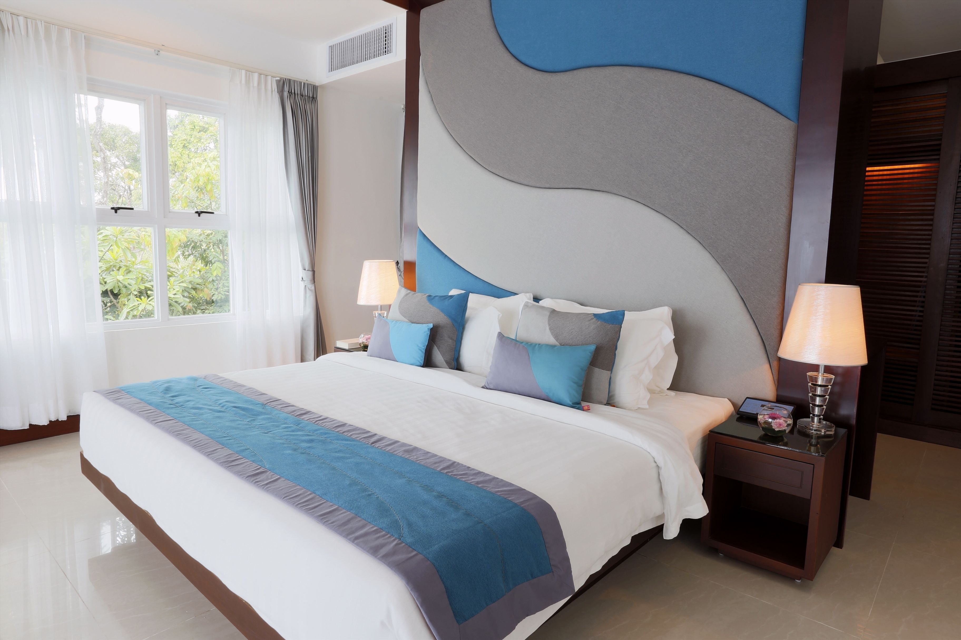 A neatly made bed with a blue and grey bedspread, two bedside lamps, and a nightstand with a lamp.