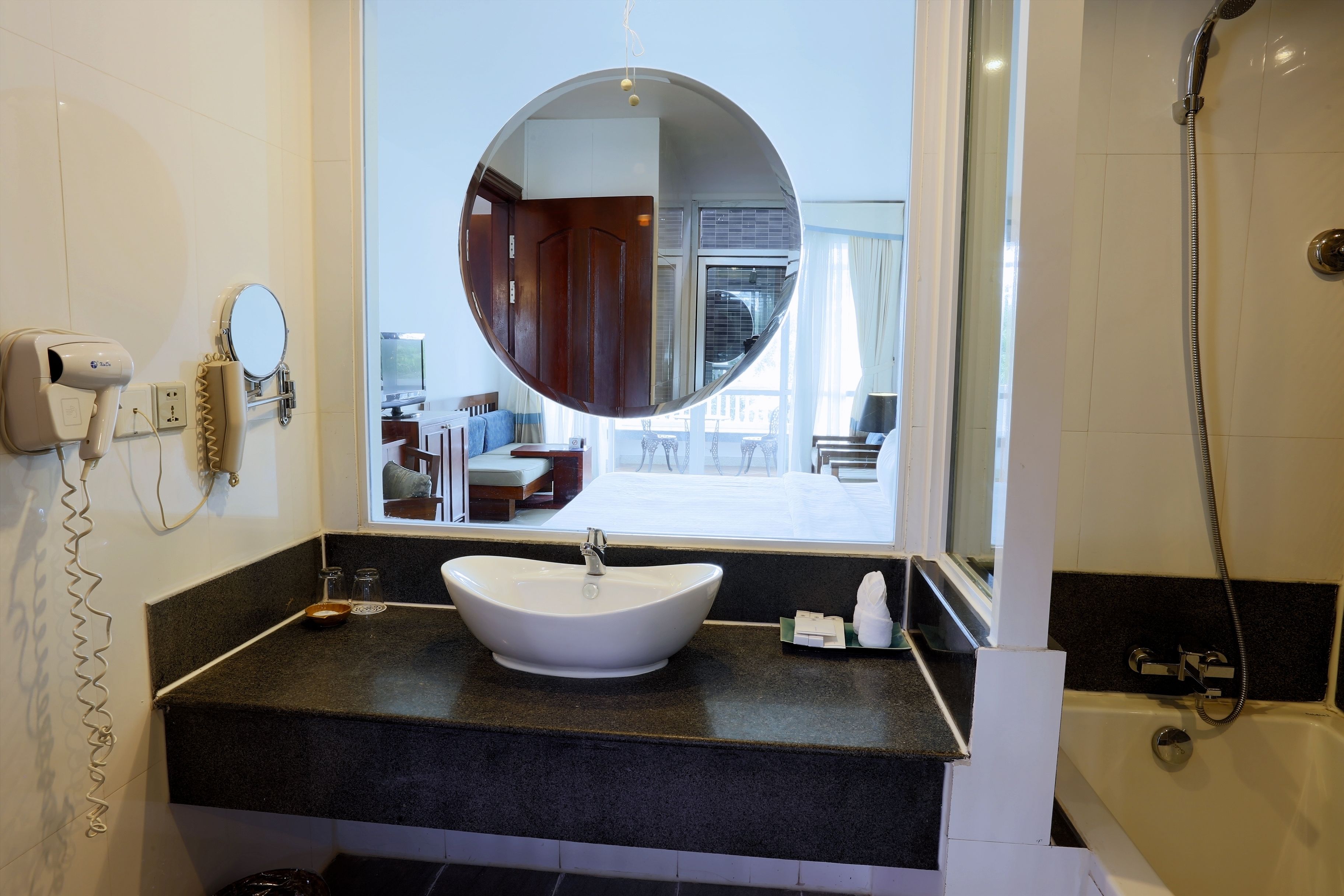 Une salle de bain avec un miroir rond, un lavabo blanc, un sèche-cheveux et une douche.