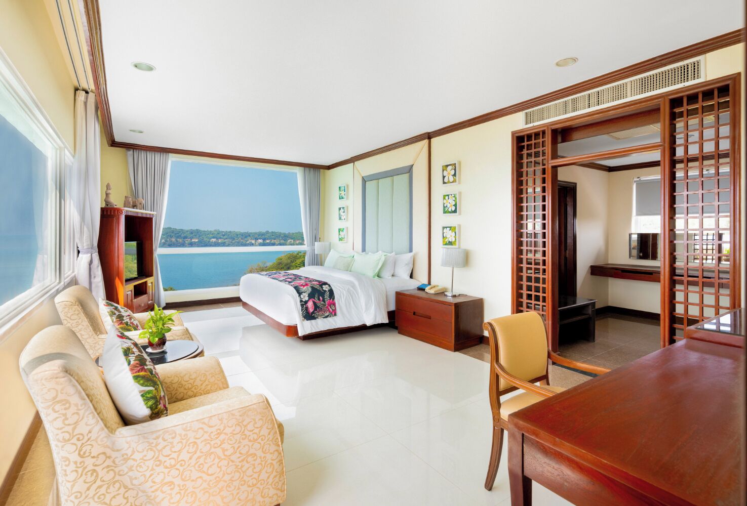 Ein Hotelzimmer mit Bett, Schreibtisch, Stuhl, Sofa, Fernseher und Meerblick.
