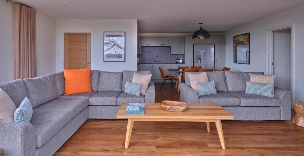 A modern living room with two grey sofas, a wooden coffee table, and a kitchen in the background.