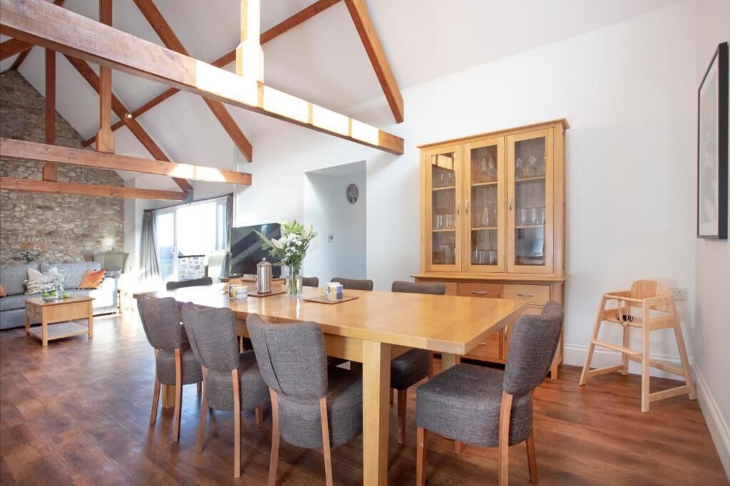 A spacious dining area with a wooden table and chairs, a stone wall, and a wooden cabinet with glass doors.