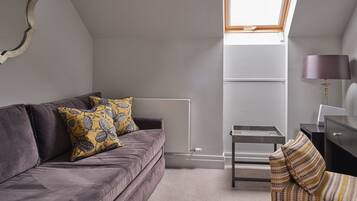 A modern loft bedroom with a grey sofa, patterned cushions, a desk with a lamp, and a skylight.