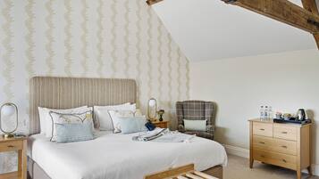 A bedroom with a large bed, a nightstand, a chair, a wooden dresser, and a wooden bench.