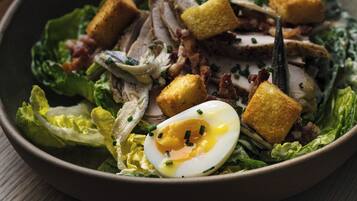 Un tazón de ensalada con lechuga, crotones, carne en rodajas y un huevo escalfado.