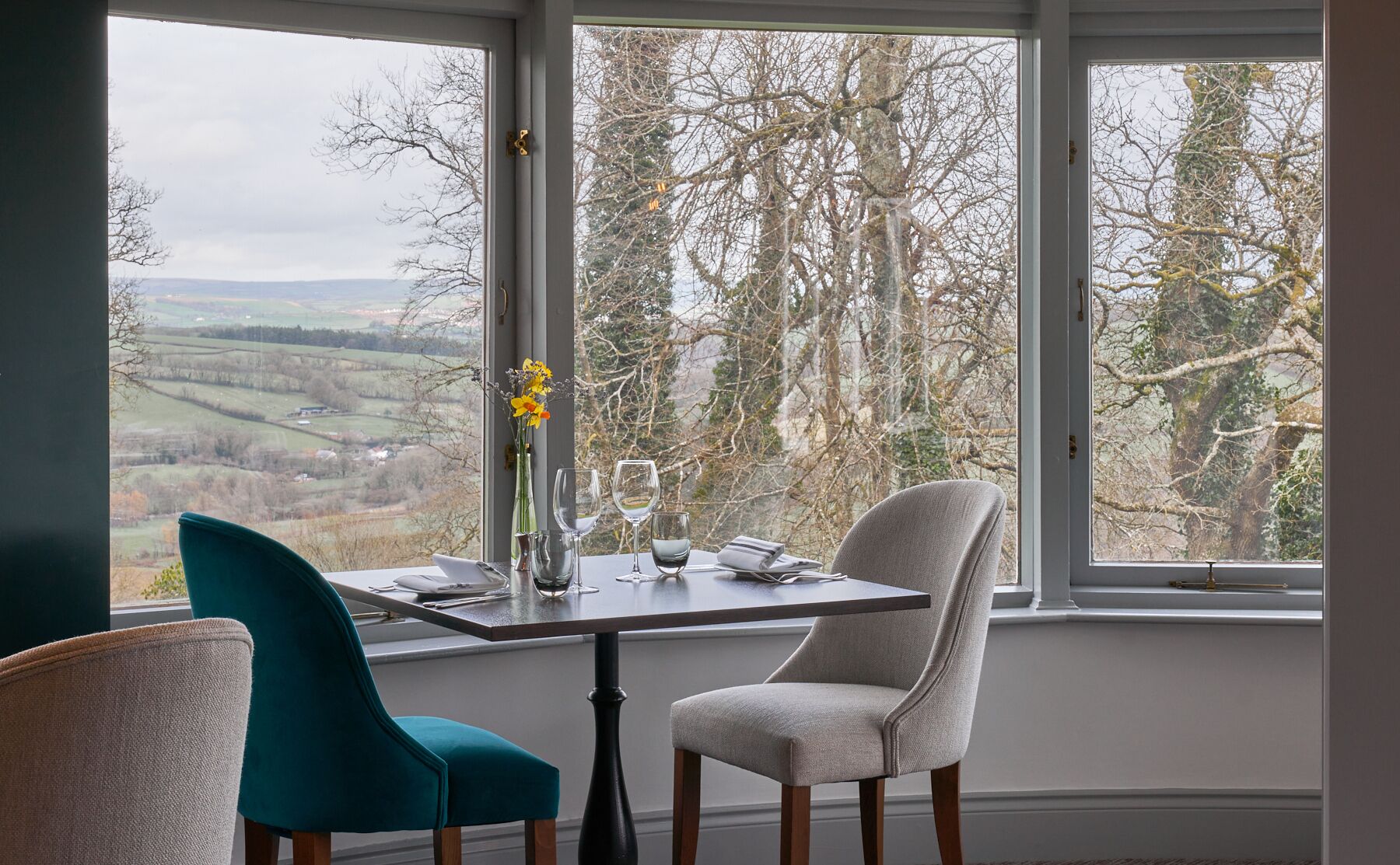 Une table à manger avec deux chaises, un vase de fleurs et des verres à vin.