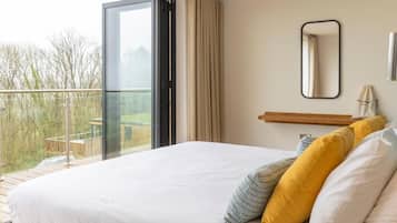A bedroom with a large bed, a sliding glass door to a balcony, a small bedside table, and a mirror on the wall.