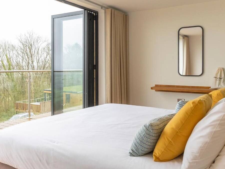A bedroom with a large bed, a sliding glass door to a balcony, a small bedside table, and a mirror on the wall.