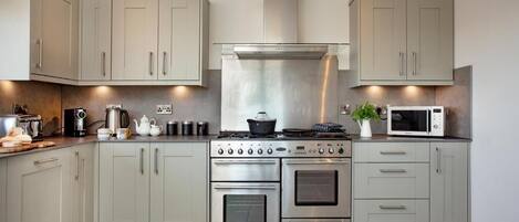 Una cocina moderna con armarios de tonos claros, una campana extractora de acero inoxidable, un microondas y una estufa a gas.
