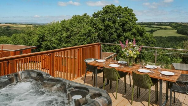 Terraza de madera con un jacuzzi, mesa de comedor para cuatro personas y vistas a colinas y árboles ondulantes.