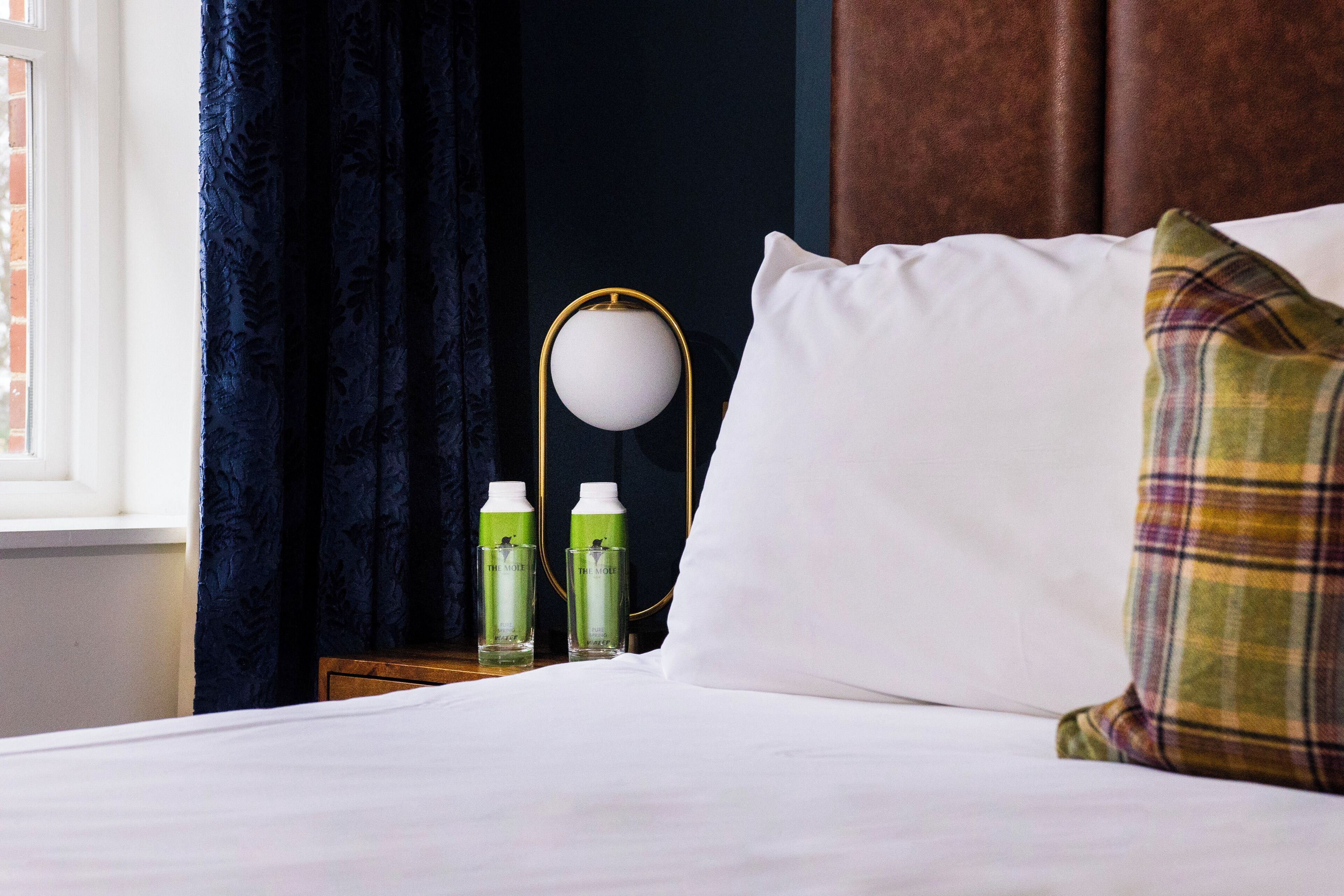 A neatly made bed with white linens, a plaid pillow, and two bottles of lotion on a bedside table.