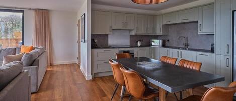 A modern kitchen with grey cabinets, a black dining table, and brown chairs.