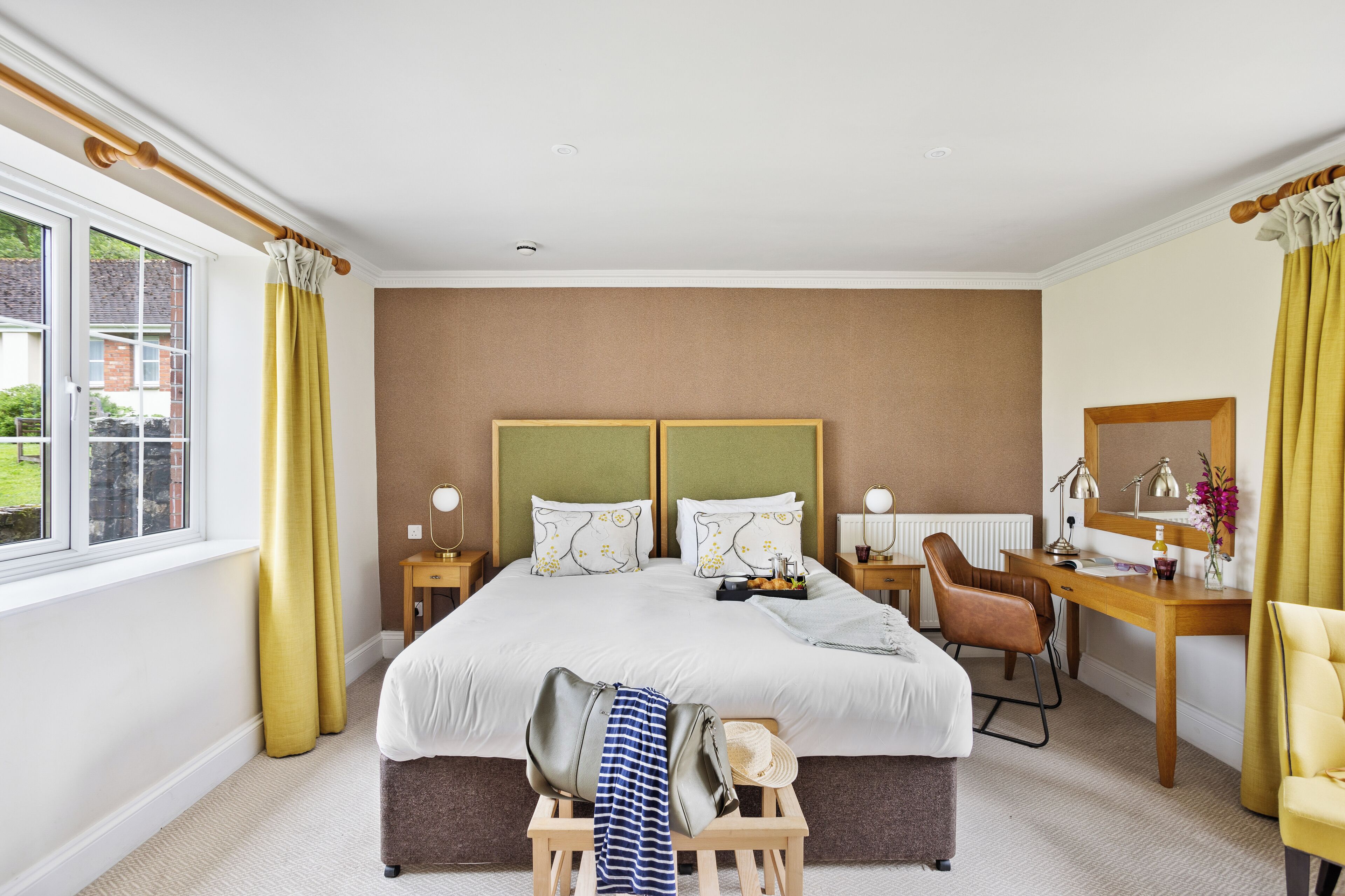 A hotel room with a large bed, two bedside tables, a desk, a chair, and a window with curtains.
