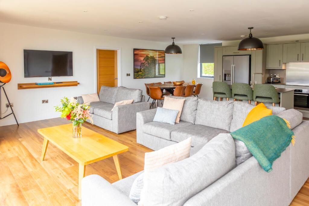 Una sala de estar moderna con sofás grises, una mesa de centro de madera y un televisor montado en la pared.