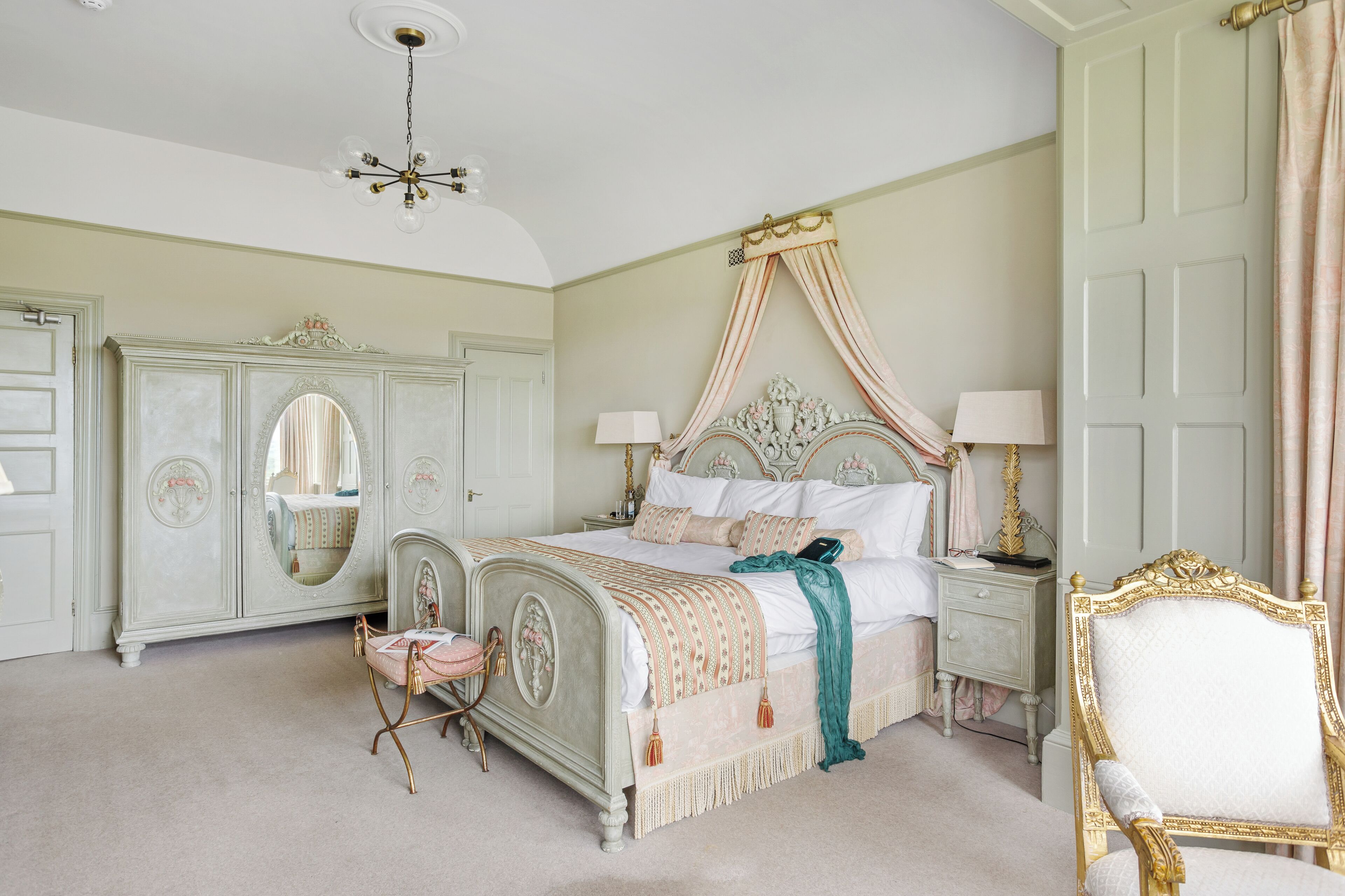 A bedroom with a four-poster bed, a vanity with a mirror, and a chair.