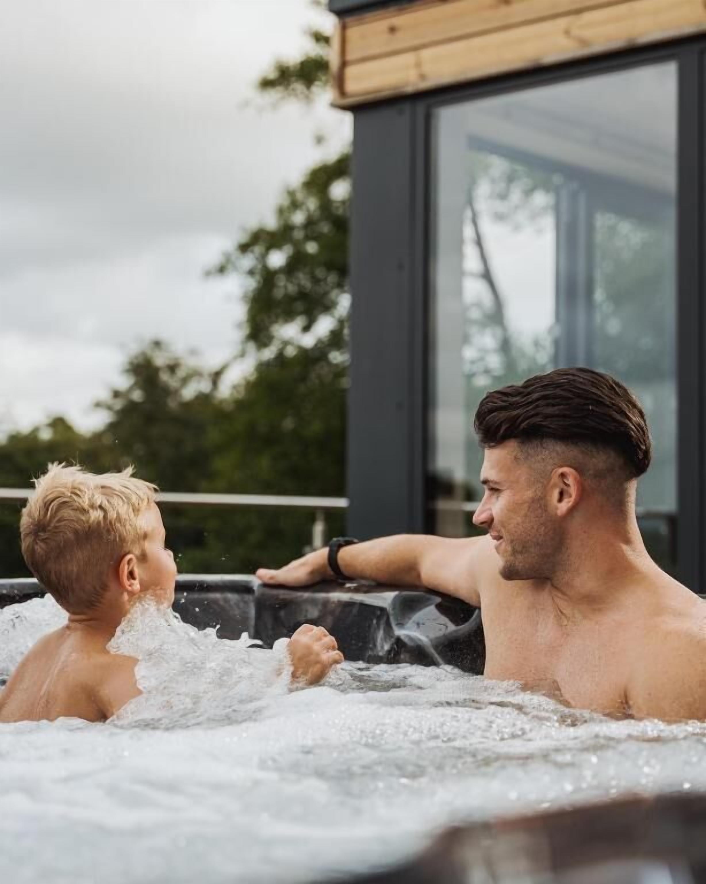 A man and a child in a hot tub with a wooden deck and a glass enclosure.