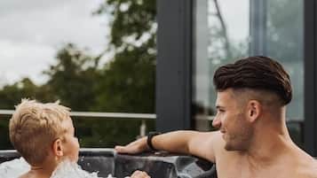 A man and a child in a hot tub with a wooden deck and a glass enclosure.