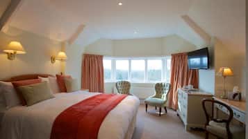A bedroom with a large bed, a dresser, a desk, two chairs, a television, and a window with curtains.