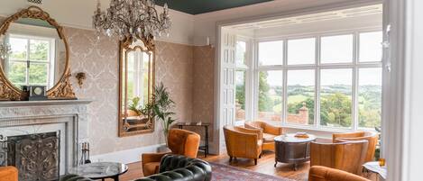 A spacious living room with a fireplace, large windows, and a chandelier.
