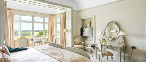 A bedroom with a large bed, a vanity with a mirror, a chair, and a view of the outdoors.
