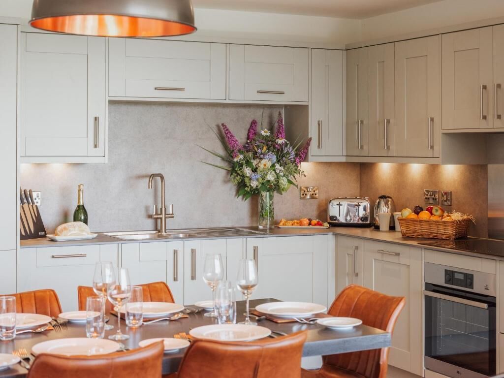 A modern kitchen with white cabinets, a central island with seating, and a dining area with orange chairs.