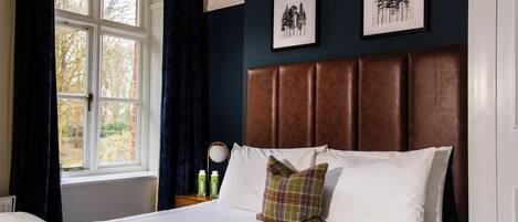A neatly made bed with white linens and a plaid pillow, a bedside table with a lamp, and two framed pictures on the wall.