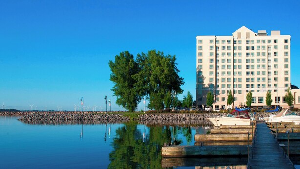 A waterfront hotel with a dock, calm water, and a large tree in the foreground. - Residence Inn by Marriott Kingston Water's Edge (Kingston)