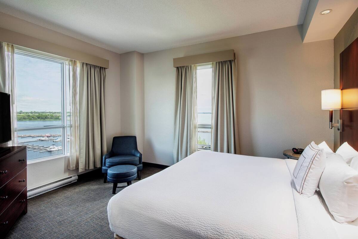 A hotel room with a large bed, a chair, a dresser, and a TV.