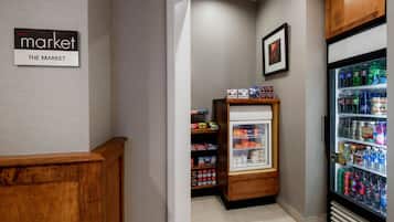 Un petit espace de vente avec un présentoir réfrigéré et des étagères remplies de collations et de boissons.