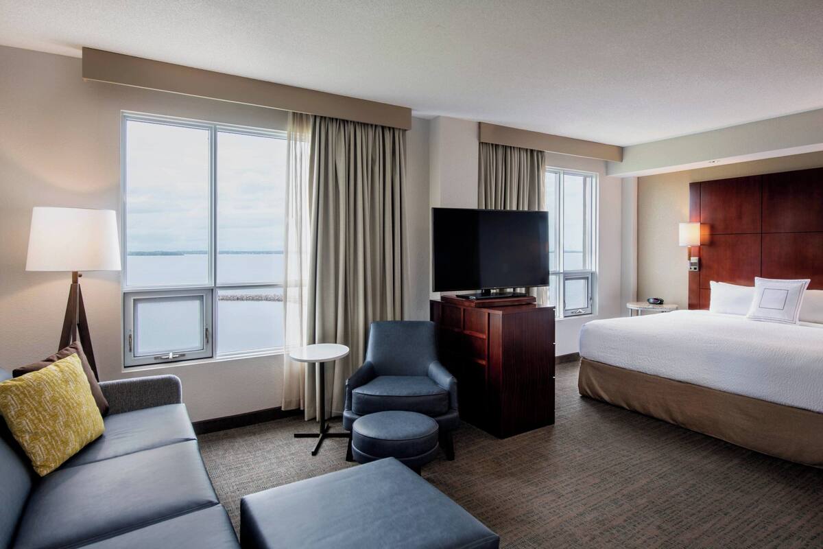 A hotel room with a large bed, a sofa, a TV, and a view of the sea.