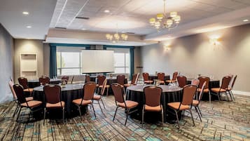 Une salle de conférence équipée de tables rondes, de chaises, d’un écran de projection et d’une grande fenêtre.