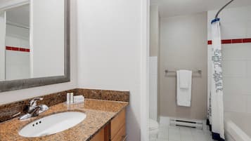 Un baño con lavamanos de encimera de granito, un espejo, ducha con cortina blanca y una toalla colgada en la pared.