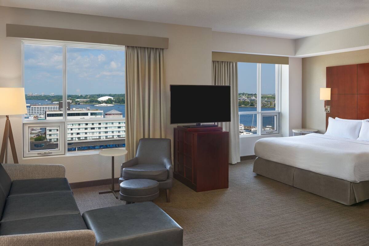 A hotel room with a bed, a TV, a sofa, and a view of the city and water.