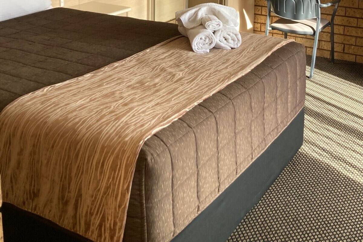 A hotel room with a brick-patterned wall, a bed with a brown quilt, a desk with a chair, and a mirror.