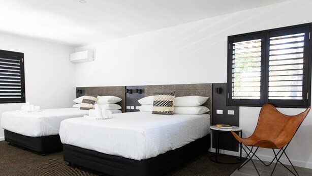 Habitación de hotel con dos camas, un sillón de cuero marrón y una mesita con un libro.