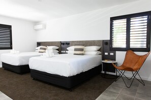 A hotel room with two beds, a brown leather chair, and a small table with a book. - Fountain View Motel (Dubbo)
