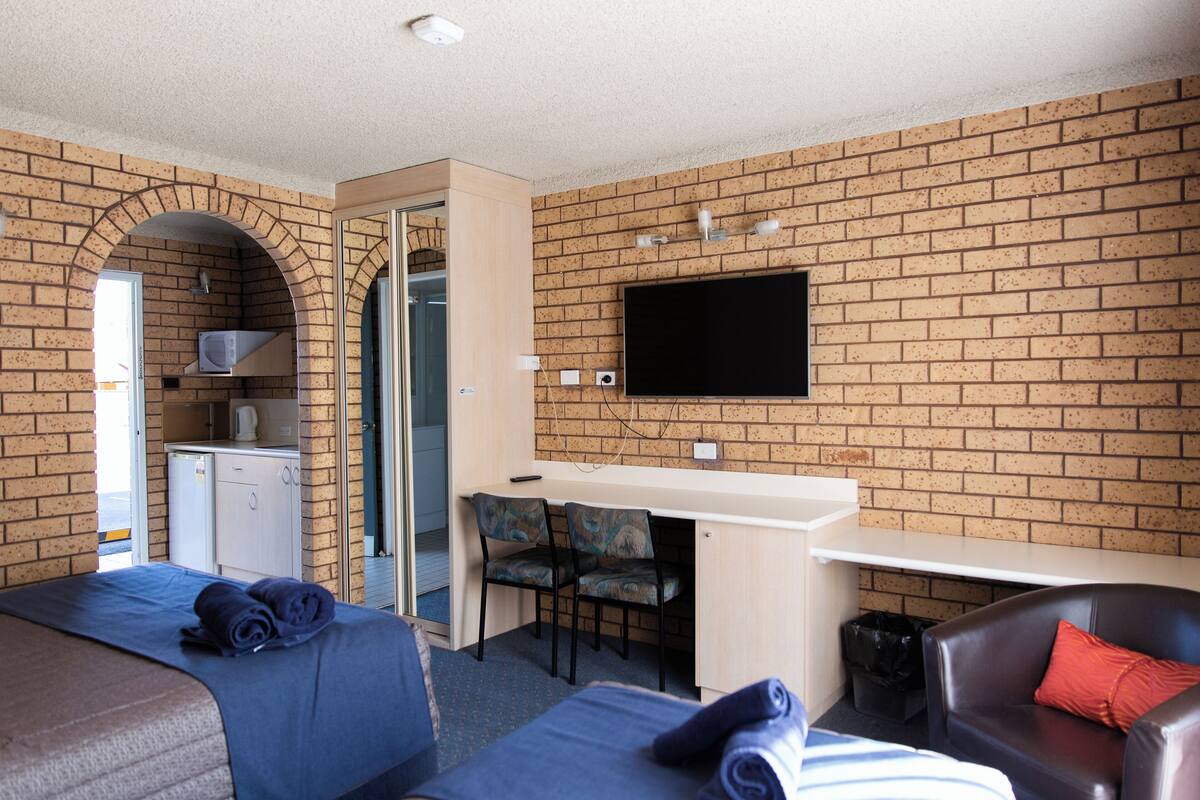 A hotel room with a brick wall, a flat-screen TV, a desk with two chairs, and two beds.
