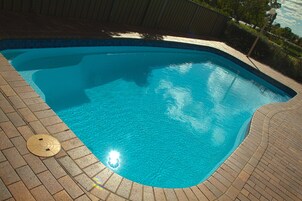 Una piscina con borde de azulejos y un reloj de sol a la izquierda.