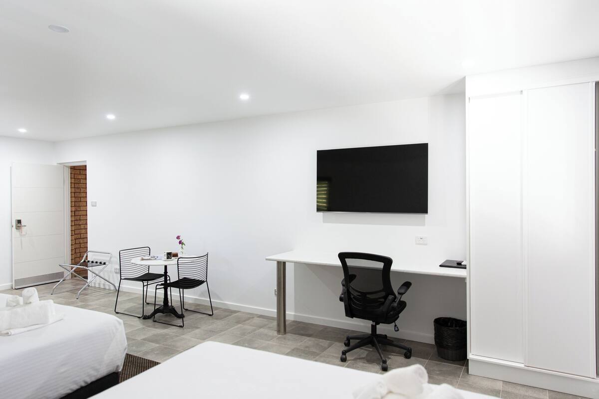 A modern hotel room with a bed, a desk, a chair, and a TV.
