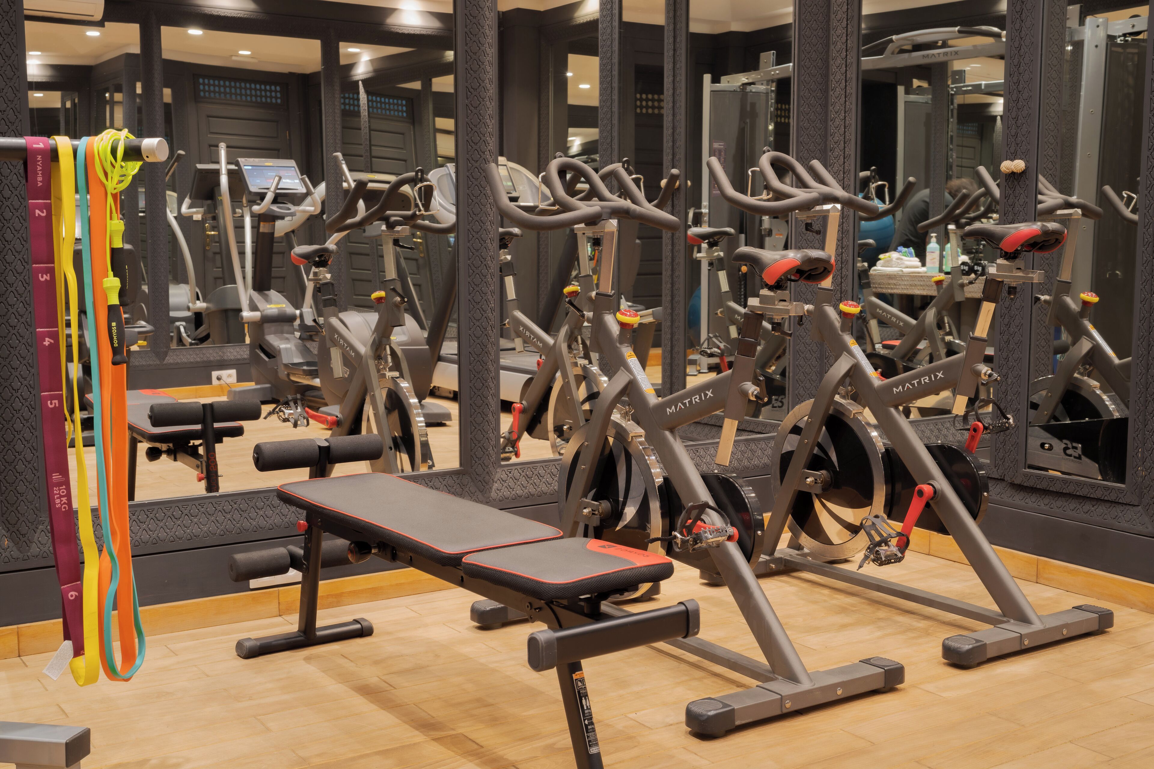 Un gimnasio con varias máquinas de ejercicio, una banca y un muro con espejos.