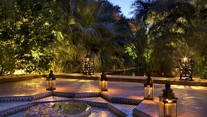 A well-lit outdoor area with a circular water feature, surrounded by palm trees and decorative lanterns. - Dar Rhizlane (Marrakech)