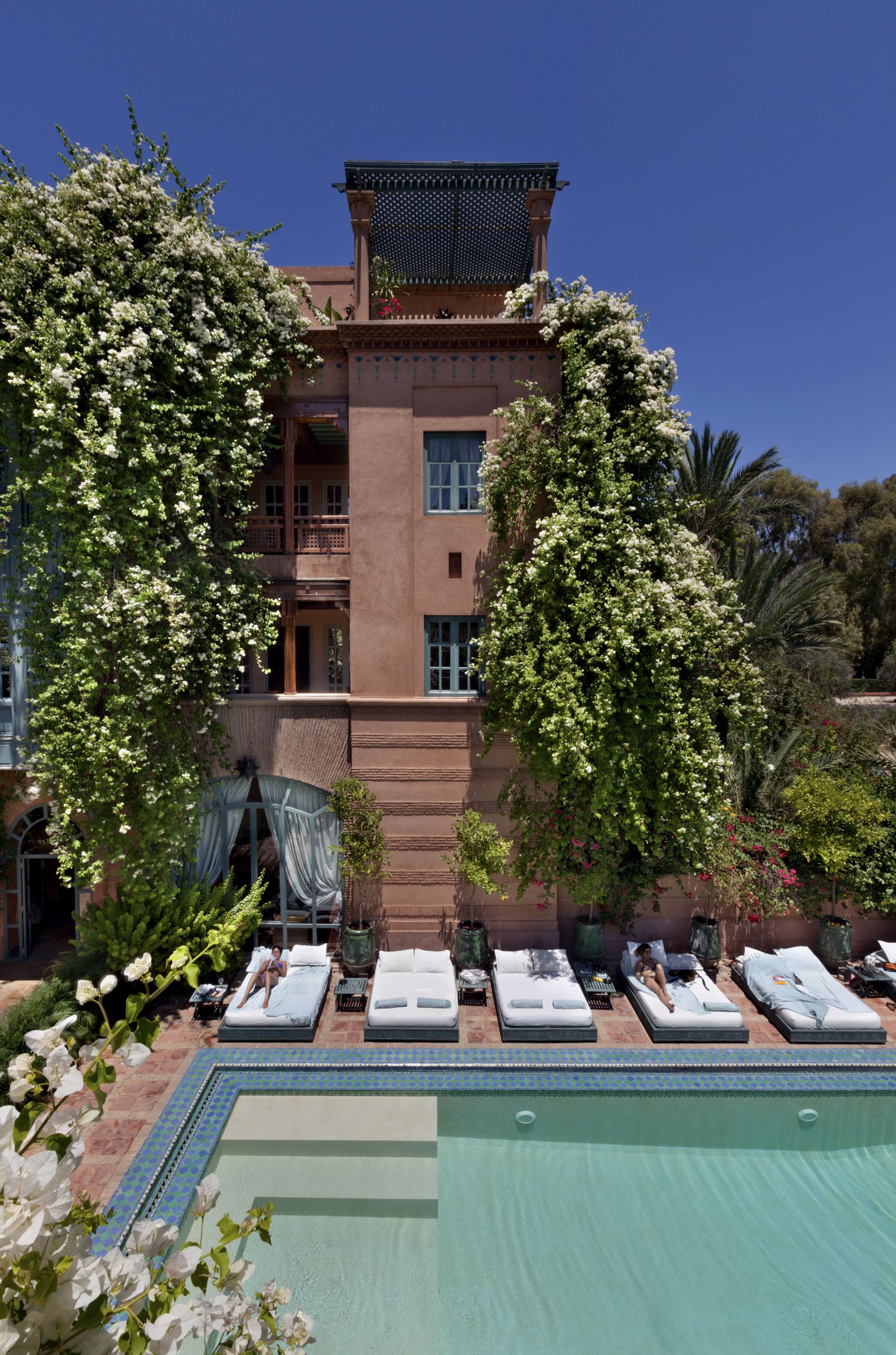 A hotel with a pool area, lounge chairs, and a building with a balcony.