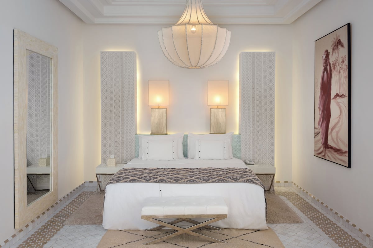 A modern bedroom with a large bed, two bedside lamps, a decorative ceiling light, and a large painting on the wall.