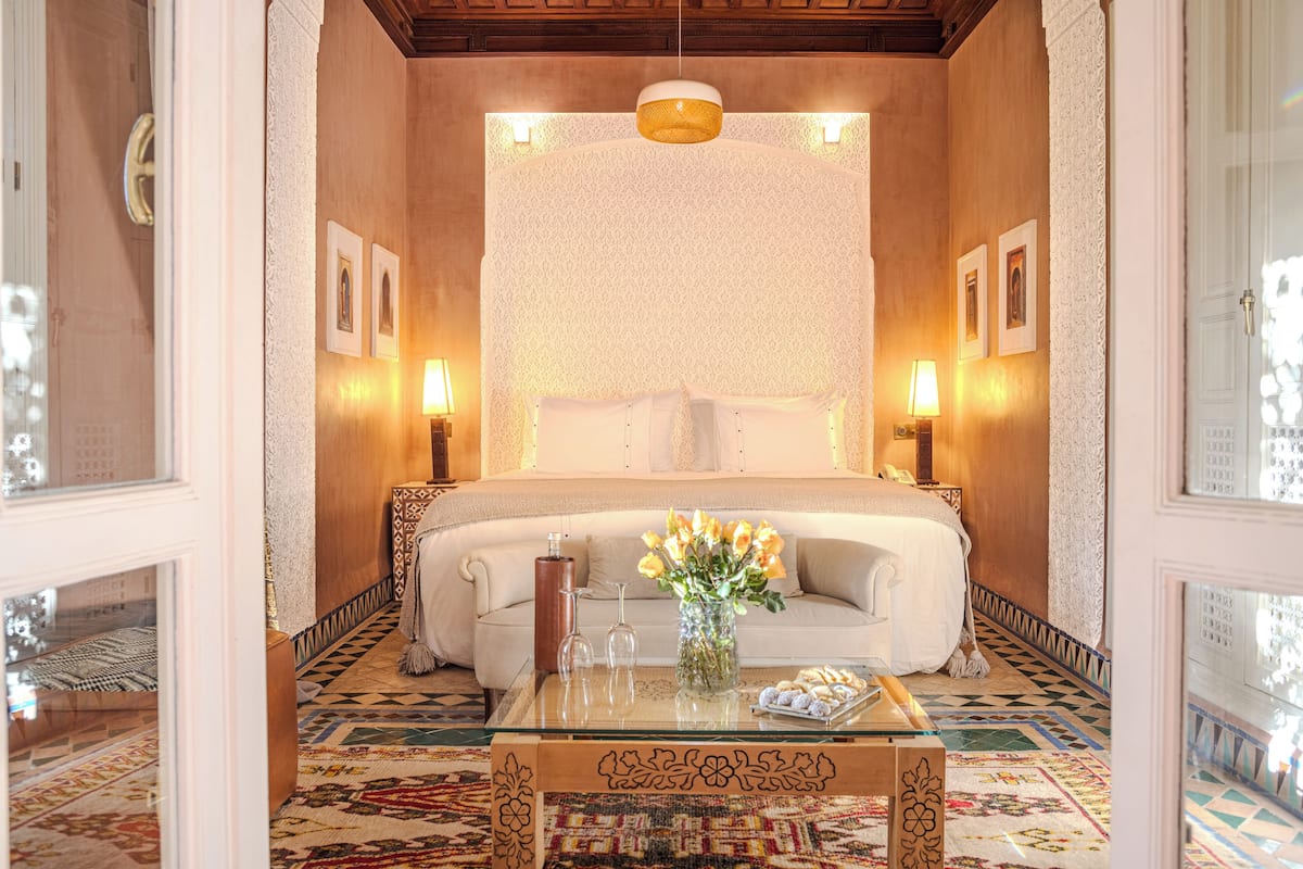 A bedroom with a large bed, a glass coffee table with a vase of flowers, and two bedside lamps.