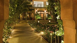 An arched pathway leading to a building with a glass facade, surrounded by lush greenery and flowering plants. - Dar Rhizlane (Marrakech)
